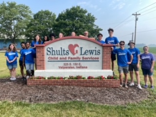 A group of people standing in front of a sign

Description automatically generated